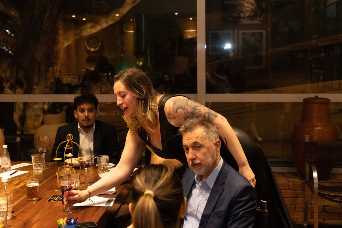 Anfitriã se inclinando sobre a mesa para conversar com um convidado